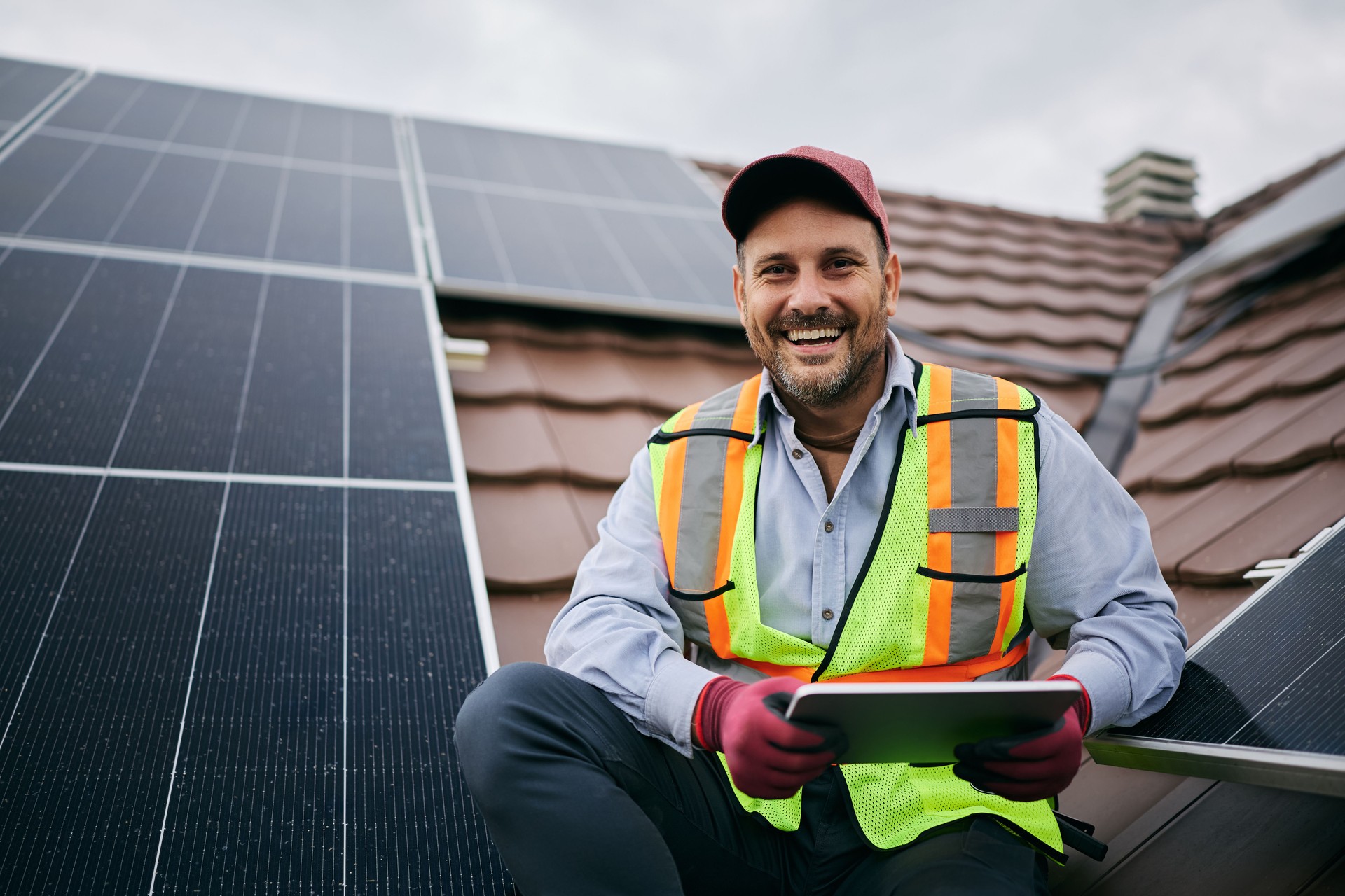 Happy solar panel engineer with touchpad on rooftop looking at camera.