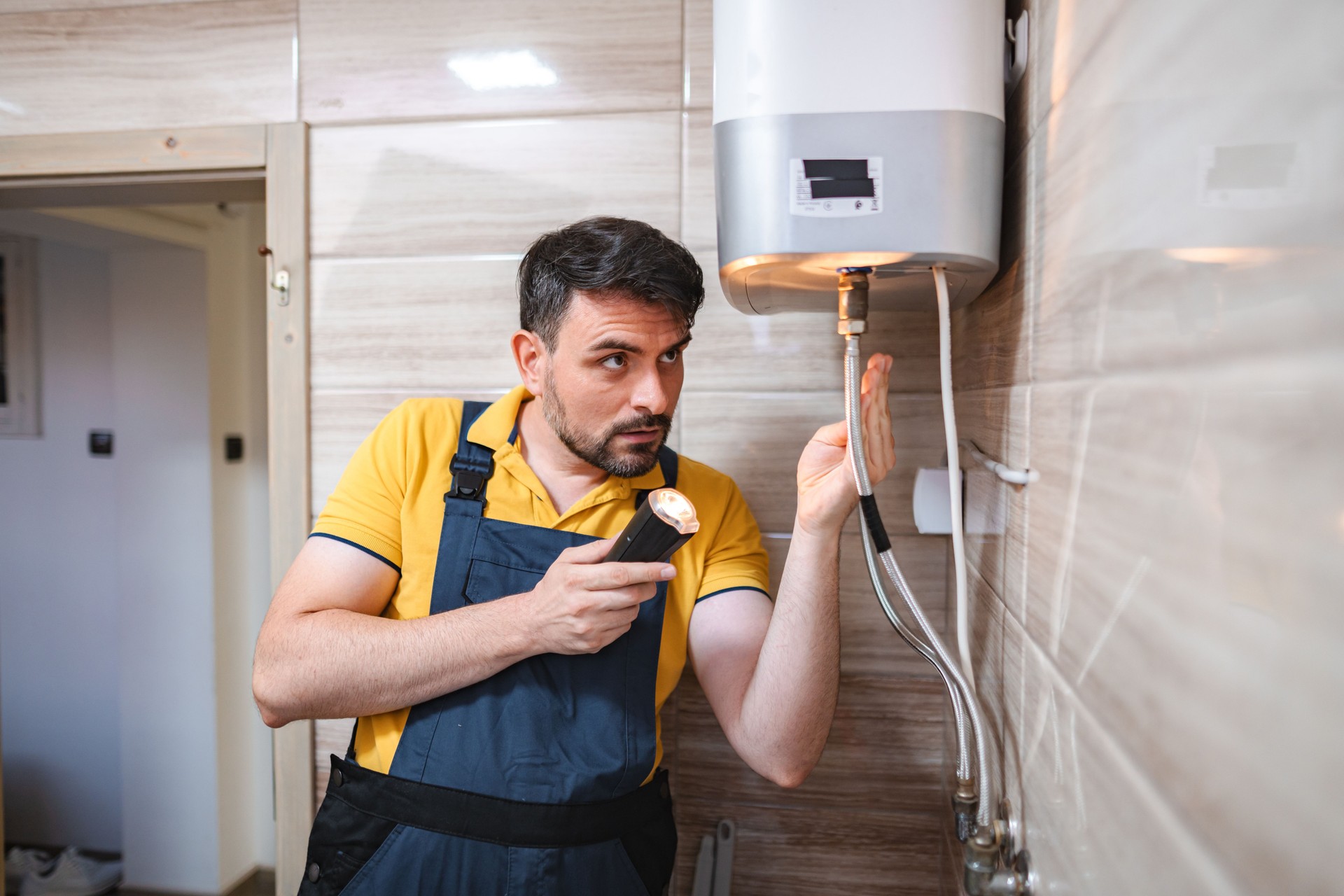 Plumber inspecting water heater with flashlight in bathroom